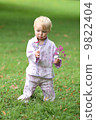 Adorable baby girl in beautiful kimono set is standing in a park with flowers in her hand  9822404