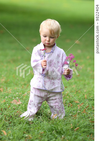 Adorable baby girl in beautiful kimono set is standing in a park with flowers in her hand Adorable baby girl in beautiful kimono set is standing in a park with flowers in her hand 9822404