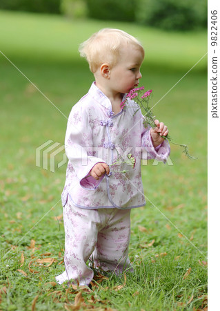 Adorable baby girl in beautiful kimono set is standing in a park with flowers in her hand  9822406