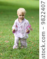 Adorable baby girl in beautiful kimono set is standing in a park with flowers in her hand  9822407