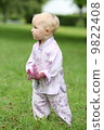 Adorable baby girl in beautiful kimono set is standing in a park with flowers in her hand  9822408
