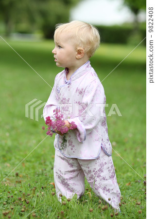 Adorable baby girl in beautiful kimono set is standing in a park with flowers in her hand Adorable baby girl in beautiful kimono set is standing in a park with flowers in her hand 9822408