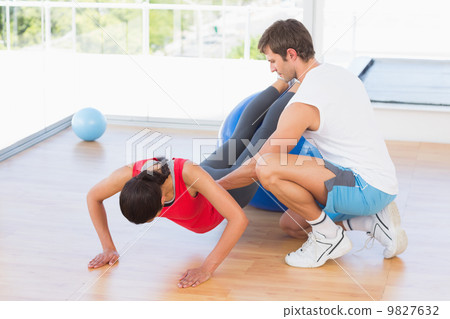 Trainer helping young woman with fitness ball at gym Trainer helping young woman with fitness ball at gym 9827632