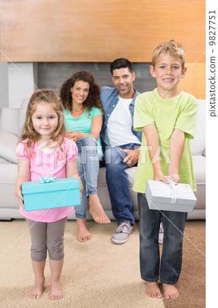 Happy siblings showing presents in front of parents on the couch Happy siblings showing presents in front of parents on the couch 9827751