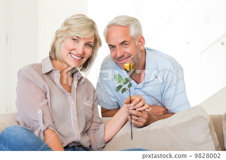 Man giving flower to a smiling woman sitting on couch Man giving flower to a smiling woman sitting on couch 9828002