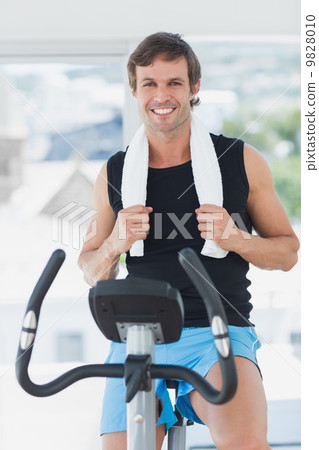 Smiling man working out at spinning class in bright gym 9828010