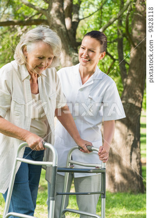 Female assisting mature woman with walker at park 9828118