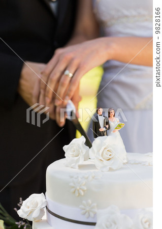 Mid section of a newlywed cutting wedding cake 9828166