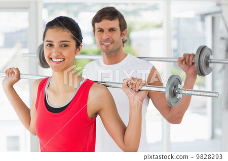 Fit young couple lifting barbells in gym 9828293
