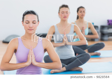 Women in Namaste position with eyes closed at fitness studio 9828564