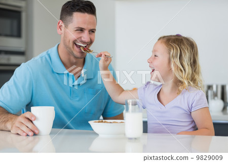 Daughter feeding cereals to father at table Daughter feeding cereals to father at table 9829009