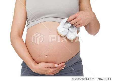 Pregnant woman holding baby shoes over bump 9829011