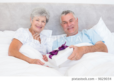 Senior man giving gift to wife in bed Senior man giving gift to wife in bed 9829034