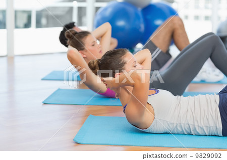 Determined people doing sit ups in fitness studio 9829092