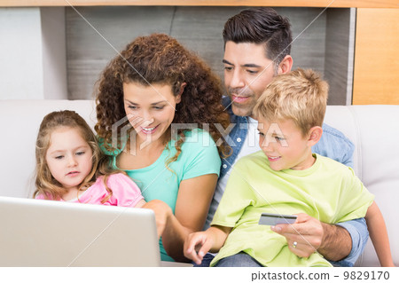 Cheerful family sitting on sofa with laptop shopping online 9829170