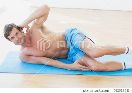 Smiling shirtless young man exercising in fitness studio Smiling shirtless young man exercising in fitness studio 9829258