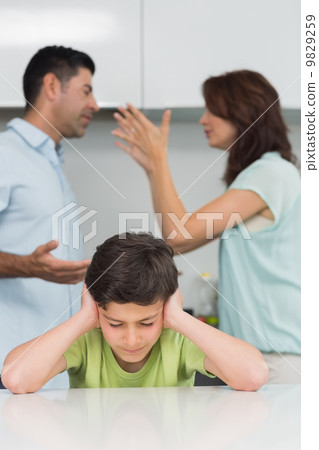Boy covering ears while parents quarreling in kitchen Boy covering ears while parents quarreling in kitchen 9829259