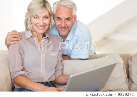 Happy mature couple using laptop on sofa 9829273