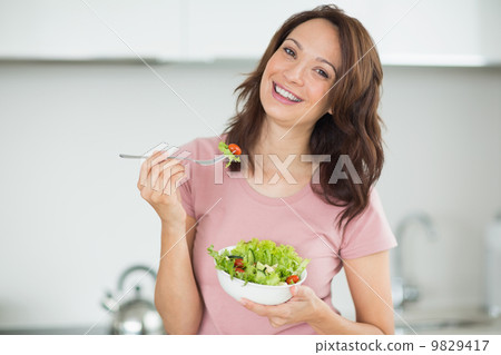 Portrait of smiling woman with a bowl of salad in kitchen 9829417