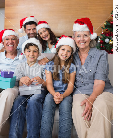 Extended family in Christmas hats with gift boxes in living room 9829453