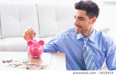 Handsome businessman putting coins into piggy bank 9829454