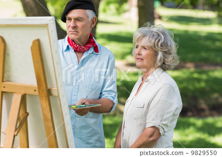 Woman watching mature man paint in park Woman watching mature man paint in park 9829550
