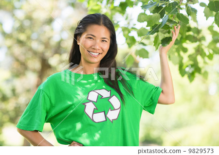 Woman in green recycling t-shirt touching leaves at park 9829573