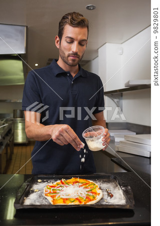 Pizza chef sprinkling cheese over pizza Pizza chef sprinkling cheese over pizza 9829801