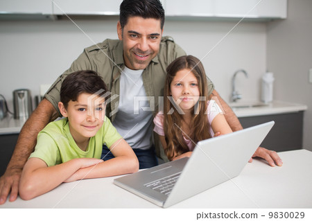 Smiling father with kids using laptop in kitchen 9830029