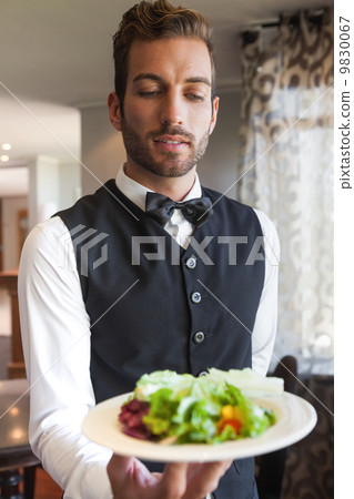 Waiter showing bowl of salad to camera 9830067