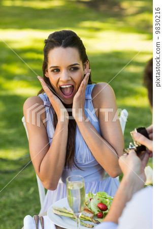 Man proposing shocked woman at an outdoor cafÃ© 9830216