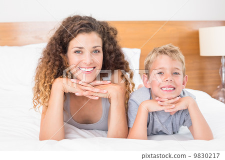 Cheerful mother and son lying on bed looking at camera Cheerful mother and son lying on bed looking at camera 9830217
