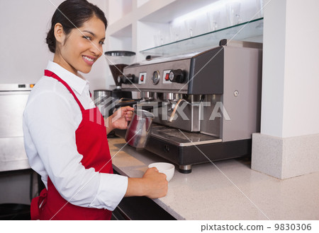 Pretty barista pouring milk into cup of coffee smiling at camera Pretty barista pouring milk into cup of coffee smiling at camera 9830306