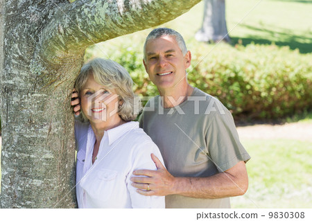 Smiling mature couple besides tree at park Smiling mature couple besides tree at park 9830308