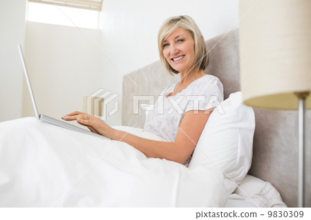 Portrait of a smiling woman using laptop in bed 9830309