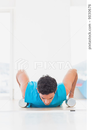 Man doing push ups with dumbbells in fitness studio Man doing push ups with dumbbells in fitness studio 9830676