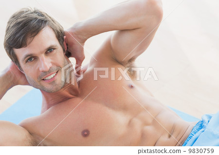 Portrait of a smiling shirtless young man doing sit ups 9830759