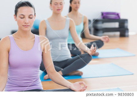 Women in lotus posture with eyes closed at fitness studio Women in lotus posture with eyes closed at fitness studio 9830803