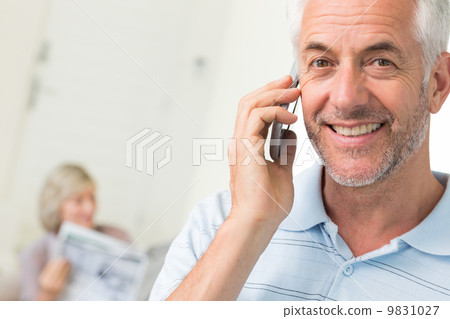Man using cellphone with woman reading newspaper at home Man using cellphone with woman reading newspaper at home 9831027