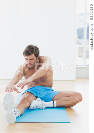 Sporty man stretching hands to leg in fitness studio 9831120