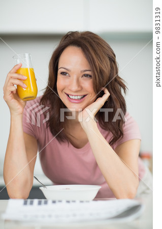 Woman with a bowl of cereals, orange juice and newspaper in kitc Woman with a bowl of cereals, orange juice and newspaper in kitc 9831319