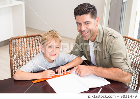 Smiling father helping son with homework at table 9831479