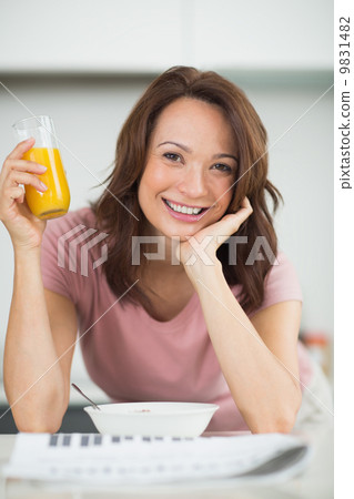 Woman with a bowl of cereals, orange juice and newspaper in kitc Woman with a bowl of cereals, orange juice and newspaper in kitc 9831482