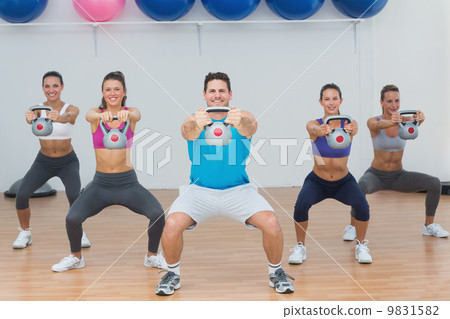 Class and instructor exercising with kettlebells in gym 9831582