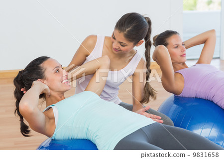 Trainer helping young woman with fitness ball 9831658