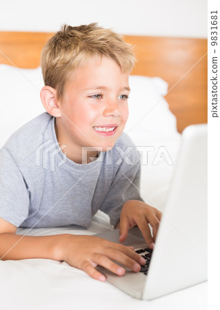 Blonde boy lying on bed using laptop Blonde boy lying on bed using laptop 9831681