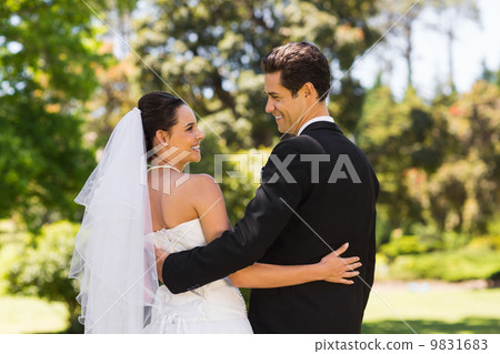 Newlywed couple with arms around in park 9831683
