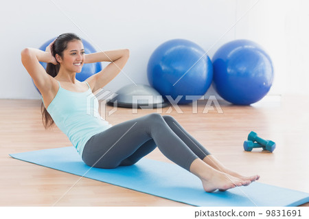 Smiling woman doing sit ups in fitness studio 9831691