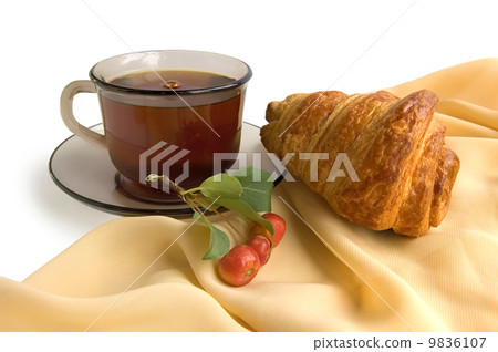 Brown glass cup with tea and croissants 9836107