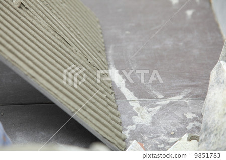 Construction worker is tiling at home tile floor adhesive 9851783